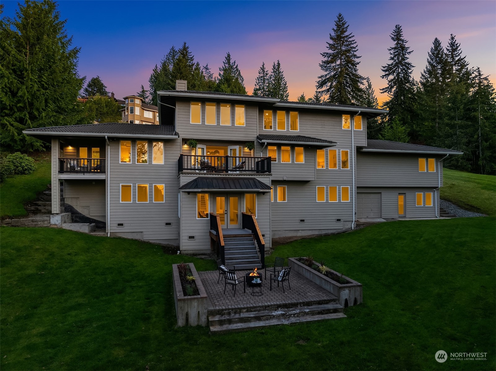 A Pacific Northwest home at twilight, warmly lit against evergreens